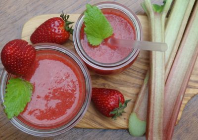 Frische Rhabarbersirup mit Erdbeeren und Minzblättern in Gläsern, perfekt für sommerliche Getränke.
