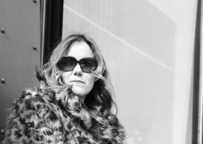 Elegante Frau mit Sonnenbrille und Fellmantel vor modernen Gebäudefassaden, Stilvolle Mode, Street Style, Modeerscheinung, Lifestyle-Foto.