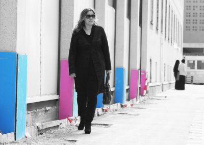 Beiläufige Frau in schwarzen Kleid mit Sonnenbrille auf Stadtstraße, bunte Akzentwände, modernes urbanes Umfeld, Streetstyle, Lifestyle, City-Mode, unabhängige Frau, Trendy Shopping, urbane Atmosphäre.