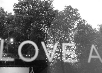 Verwitterte Glasscheibe mit reflektierenden Baumdetails hinter einer LOVE-Schriftzug.