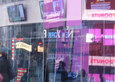 Innenstadt reflektierende Glasfassade mit digitalen Werbetafeln und Neon-Schildern, urbanes Stadtbild in New York, lebhafte Atmosphäre mit Passanten und leuchtenden Anzeigen, modernes Hochhaus-Design, typische Szenerie für City-Fotografie.