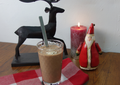 Süßer Schokoladenkuchen im Glas mit einem Löffel, festliche Weihnachtsdeko mit Kerzen, Engel und Schneemann, auf rustikaler Holzplatte, für festliche Backkunst und Weihnachtsdekoration, bei Sono Cats.