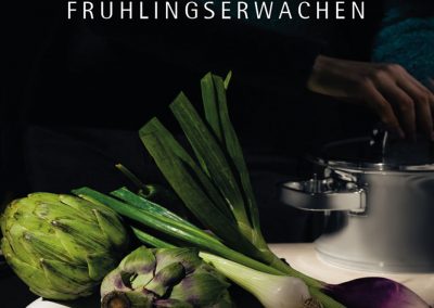 Frühlingserwachen mit frischen Artischocken, Frühlingszwiebeln und Lauch in modernem weißen Obstteller auf Küchentheke, symbolisiert saisonale Gemüsesorten für gesunde Ernährung.