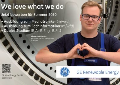 Motivierter Auszubildender zum Mechatroniker bei GE Renewable Energy, der in einer technischen Umgebung lächelnd mit Herzform die Hände formt.