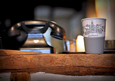 Kaffeetasse mit Grafrath-Stadtmotiv auf hölzernem Tisch, neben retro Telefon, gemütliche Atmosphäre im Café, perfekte Szenerie für Kaffeegenuss und Entspannung.